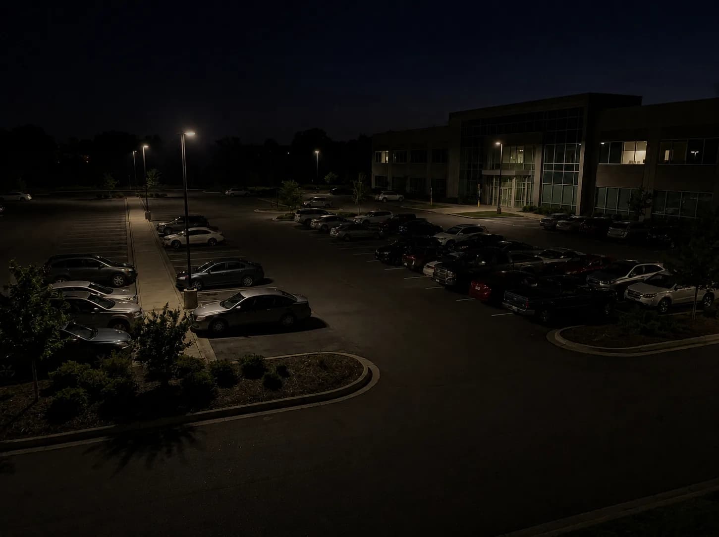 Estacionamento à noite com poucos postes, poças de luz e grande parte do pátio em sombra